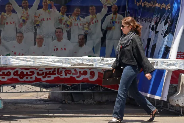 A woman walks past a banner bearing images of the members of Iranian national volleyball team, erected along a street at the Vanak Square in Tehran on June 10, 2026. (Photo by ATTA KENARE / AFP) 