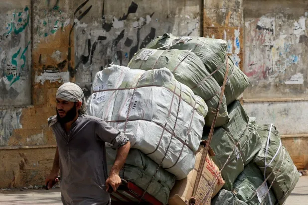 عامل يسحب عربة محملة بالبضائع لتوصيلها إلى سوق قريبة في كراتشي بباكستان (رويترز)