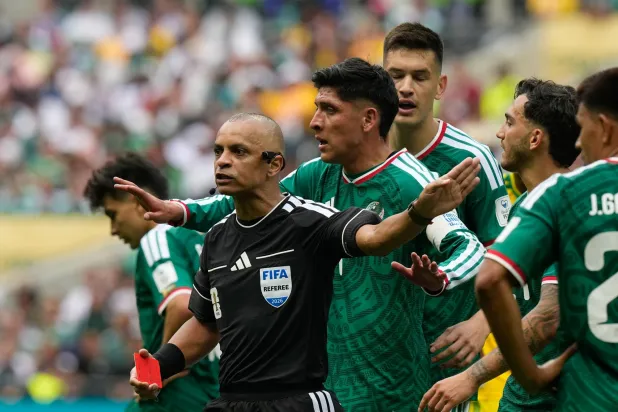 يحتج لاعبو المنتخب المكسيكي لدى الحكم البرازيلي ويلتون سامبايو بعد إشهاره البطاقة الحمراء في وجه المدافع سيزار مونتيس (أ.ب)
