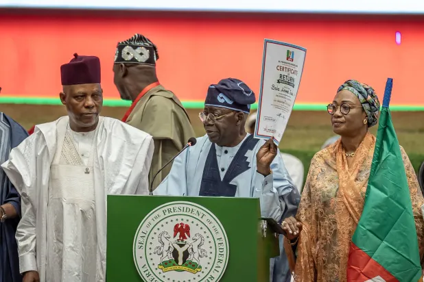 Nigeria's President Bola Ahmed Tinubu (C) displays his certificate of return as the flag bearer of his party after emerging victorious during the All Progressive Congress (APC) presidential primary election at the Bola Ahmed Tinubu International Conference Center on May 24, 2026. (Photo by Light Oriye Tamunotonye / AFP)