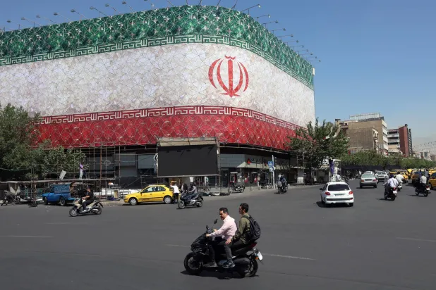 Iranians drive past a billboard featuring Iran's national flag at Enqelab Square in Tehran, Iran, 14 June 2026. EPA/ABEDIN TAHERKENAREH 