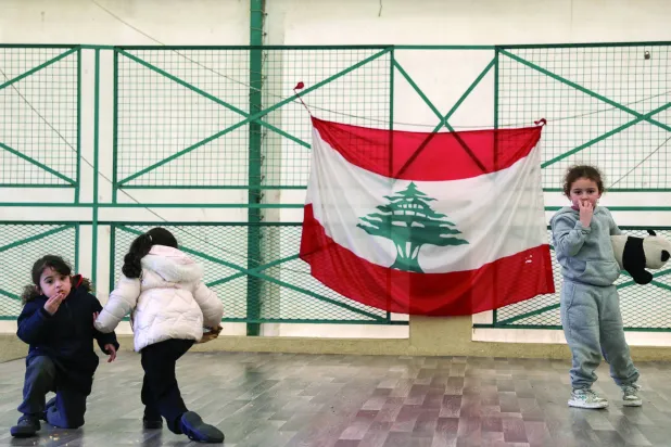 أطفال نازحون يلعبون في مدرسة تحولت إلى مركز للنزوح ومن خلفهم العلم اللبناني (رويترز)