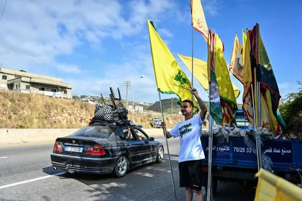 Displaced families drive past a man holding the Hezbollah party flag as they drive along the highway through the area of Jiyyeh as they return to their home villages in southern Lebanon on June 15, 2026. (AFP)