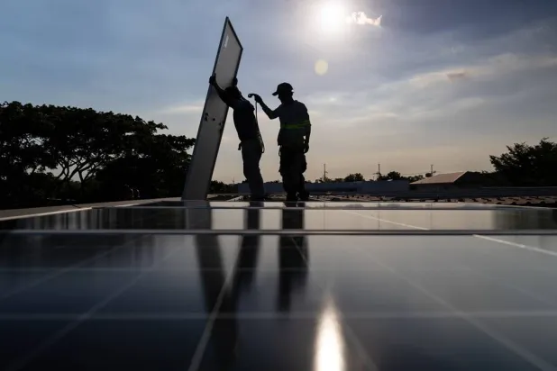 A pair of solar installers haul a solar panel onto the roof of a home in Manila, Philippines, on April 30, 2026. (AP) 