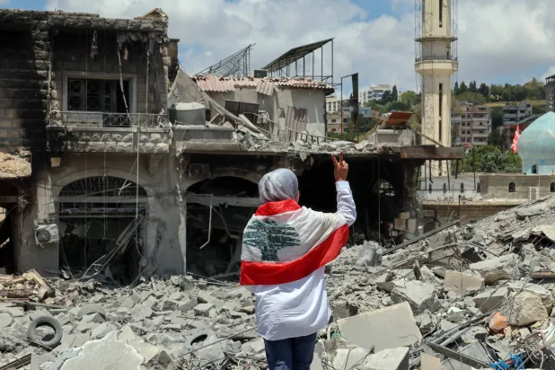 لبنانية تضع العَلَم اللبناني على كتفيها وتتفقد الدمار في ساحة مدينة النبطية بجنوب لبنان (إ.ب.أ)