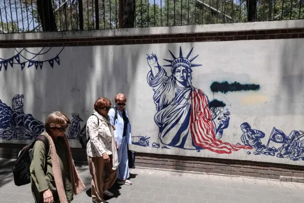  İranlı kadınlar, Tahran'daki eski ABD büyükelçiliği binasının önündeki Amerikan karşıtı duvar resminin önünden geçiyor (AFP)