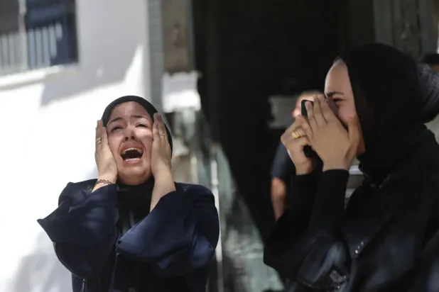 İsrail'in perşembe günü Gazze kentine düzenlediği hava saldırısında hayatını kaybeden bir kişinin cenaze töreni sırasında iki Filistinli kadın gözyaşları içinde ağıt yakıyor. (AFP)