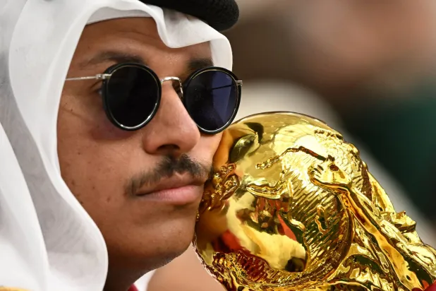 مشجع قطري ممسكاً بمجسم لكأس العالم في المدرجات (رويترز)