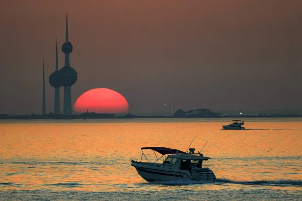 A boat sails in the Gulf waters as the sun sets behind Kuwait City's landmark Kuwait Towers on June 9, 2026. (Photo by YASSER AL-ZAYYAT / AFP)