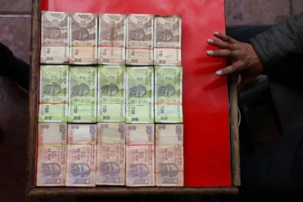 بائع يعرض أوراقاً نقدية هندية متنوعة في كشك لصرف العملات في دلهي القديمة (رويترز)