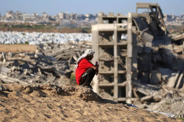 TOPSHOT - A man sits atop a hill near destroyed and heavily-damaged buildings at the Nuseirat camp for Palestinian refugees in the central Gaza Strip on June 19, 2026. (Photo by Eyad Baba / AFP)