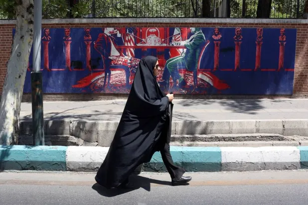 A veiled Iranian woman walks past an anti-US mural, depicting an Iranian and US negotiation table, next to the former US embassy in Tehran, Iran, 22 June 2026. (EPA)