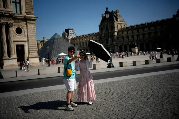 Tourists with an umbrella take a photo in Paris, Monday, June 22, 2026. (AP Photo/Christophe Ena )