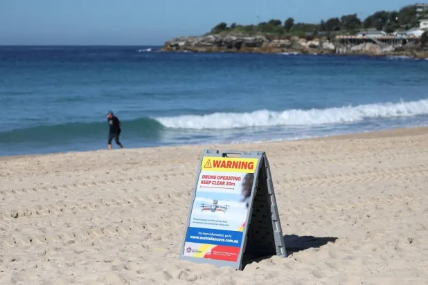 A warning sign notifying the public that a shark-spotting drone is operating in the area is displayed at Coogee Beach following a shark attack on Saturday, in Sydney, Australia, June 16, 2026. (Reuters)