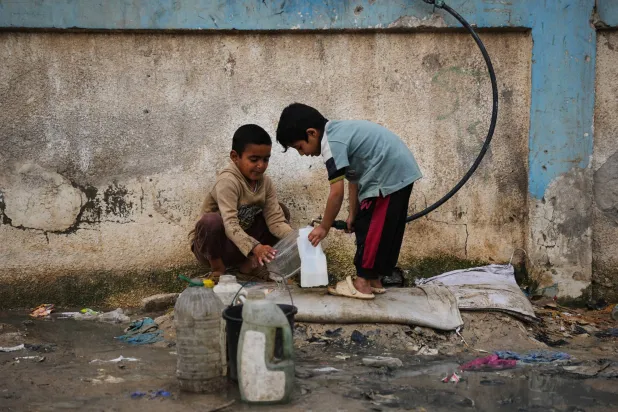 أطفال فلسطينيون يملأون عبوات بالماء في مخيم للنازحين في دير البلح بقطاع غزة (أ.ب)