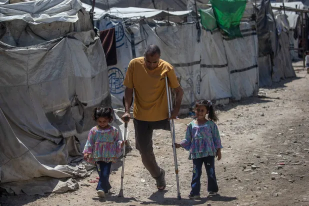 فلسطيني محرر من السجون الإسرائيلية مبتور الساق يسير مع ابنتيه في مخيم للنازحين بمدينة غزة (إ.ب.أ)