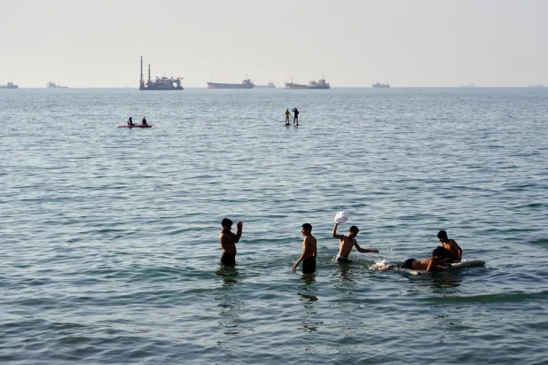 Residents swim and play in the waters of the Strait of Hormuz while cargo ships and commercial vessels lie anchored in the distance off Bandar Abbas, Iran, Wednesday, June 10, 2026.(Razieh Poudat/ISNA via AP)