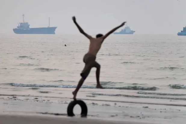 A boy balances on a tire at the water's edge as ships are seen in the Strait of Hormuz off Bandar Abbas, Iran, Tuesday, June 30, 2026 (AP) 