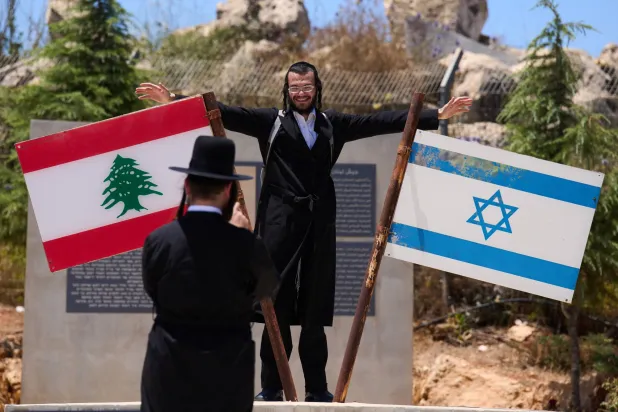 إسرائيلي متشدد يلتقط صورة قرب عَلَمَي لبنان وإسرائيل مرفوعين على نصب تذكاري في بلدة المطلة المحاذية للحدود اللبنانية (أ.ب)