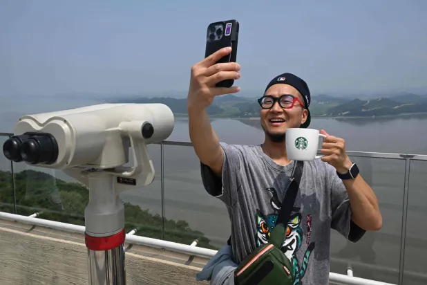 TOPSHOT - A visitor holding a Starbucks cup takes a selfie as he looks at the North Korean side from a South Korean observation deck at Aegibong Peace Ecopark in Gimpo on July 1, 2026. (Photo by Jung Yeon-je / AFP) 