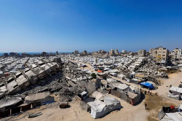  Palestinians make their way past the rubble of residential buildings destroyed during the Israeli offensive as displaced people shelter in tents, in Gaza City, July 4, 2026. (Reuters)