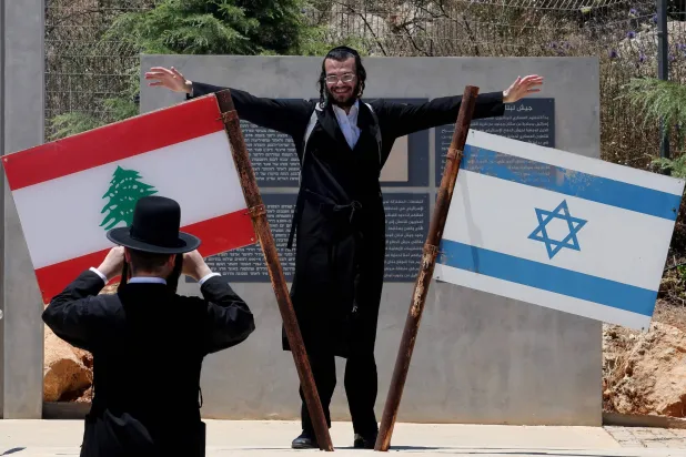 يهودي متشدد يقف بجانب العلمين الإسرائيلي واللبناني على الحدود بين البلدين (أ.ف.ب)