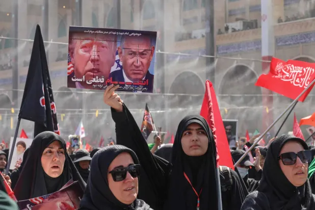 Cenaze törenine katılanlardan biri, üzerinde ABD Başkanı Donald Trump ile İsrail Başbakanı Binyamin Netanyahu'nun fotoğrafları ve "İntikam kaçınılmazdır" yazısı bulunan pankart taşıyor. (AFP)