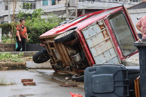A woman walks past a vehicle knocked over by winds from Typhoon Bavi in Wenling, in China's eastern Zhejiang province on July 12, 2026. (Photo by CN-STR / AFP)