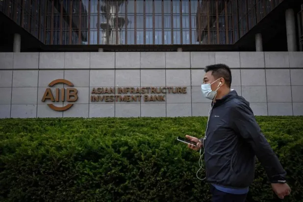 Pekin’deki Asya Altyapı Yatırım Bankası (AIIB) binasının önünden geçen bir adam (AFP)