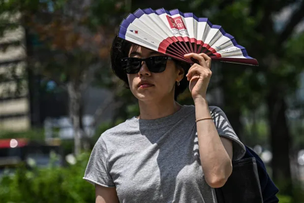A woman uses a fan to shelter from the sun on a street in Seoul on July 12, 2026. (Photo by JADE GAO / AFP)