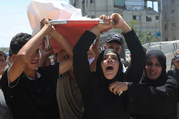 والدة الطفل الفلسطيني معتز أبو شعر الذي قُتل بنيران إسرائيلية ومشيعون يحملون جثمانه في خان يونس جنوب غزة يوم الثلاثاء (رويترز)