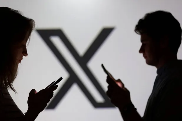 Teens pose for a photo while holding smartphones in front of the X logo. (Reuters) 