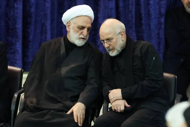 رئيس السلطة القضائية غلام حسين محسني إجئي يهمس في أذن قاليباف على هامش مراسم تأبين المرشد السابق علي خامنئي مساء الثلاثاء (البرلمان الإيراني)