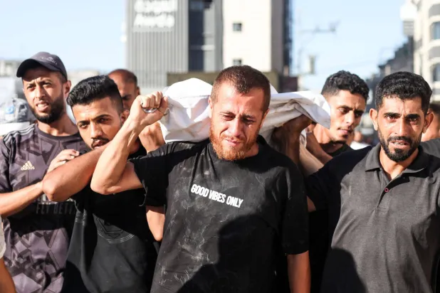 فلسطينيون يحملون جثماناً آخر قتل في غارة إسرائيلية على مخيم النصيرات (د.ب.أ)