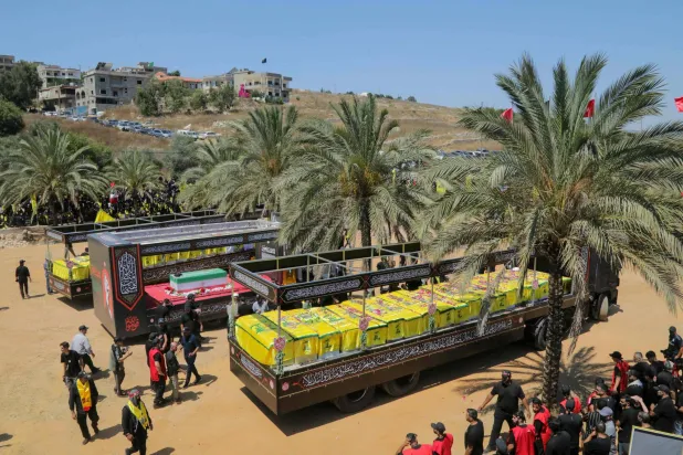 The caskets of Hezbollah fighters killed during clashes with the Israeli army are pictured to the right and left of a mock coffin of Iran's slain supreme leader, Ali Khamenei, during a mass funeral in the southern Lebanese village of Majdel Selm on July 18, 2026. (Photo by Ibrahim AMRO / AFP)