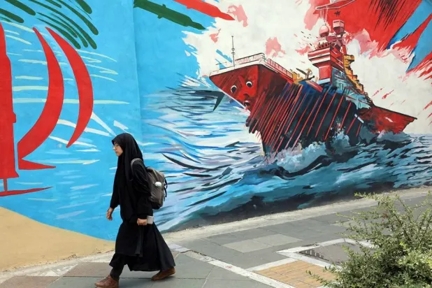 A woman walks next to anti-US graffiti on a street in Tehran, Iran, 20 July 2026. (EPA)