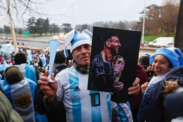 رجل يرفع صورة ليونيل ميسي في نهائي كأس العالم 2022 بينما يرحب المشجعون بالمنتخب الوطني بعد عودته من كأس العالم 2026 (إ.ب.أ)