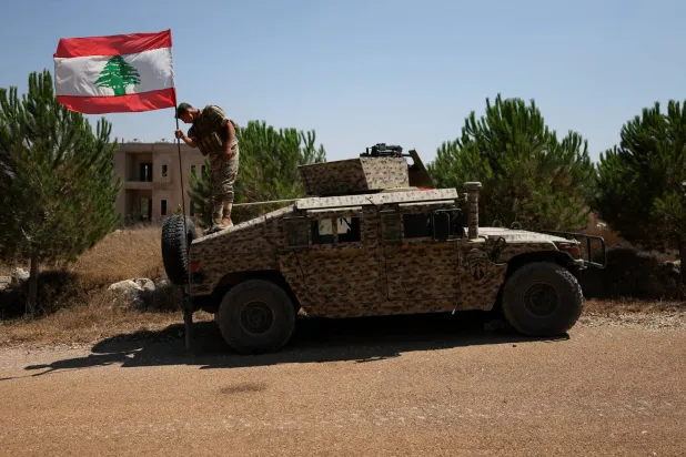 يرفع أحد الجنود اللبنانيين العلم اللبناني على آلية مدرعة في بلدة زوطر الغربية بجنوب لبنان بالتزامن مع انتشار وحدات الجيش في المنطقة عقب انسحاب القوات الإسرائيلية ضمن المرحلة الأولى من تنفيذ الخطة المدعومة أميركياً (رويترز)