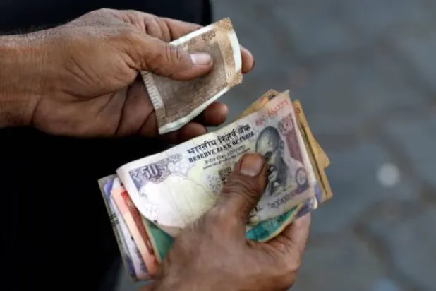 أمين صندوق يمسك أوراقاً نقدية هندية في محطة وقود بمدينة أحمد آباد (رويترز)