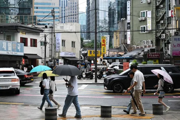 People carry umbrellas as they walk along a sidewalk in Seoul on July 21, 2026. (AFP)