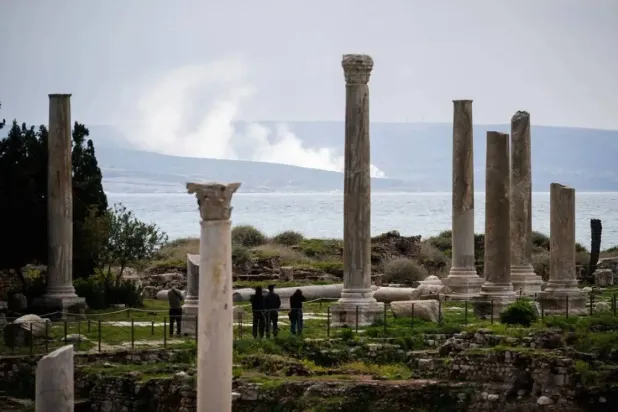 23 Mart 2026'da çekilen bir fotoğraf, Lübnan'ın güneyindeki Sur (Tyre) kentinde bulunan Fenike limanı arkeolojik alanının arkasındaki İsrail hava saldırısı bölgesinden yükselen dumanı gösteriyor (AFP)