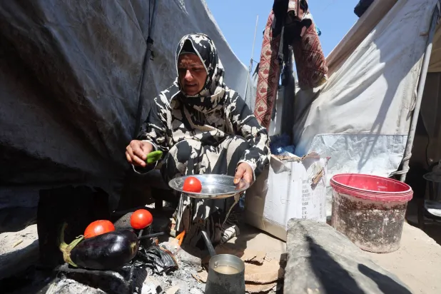 Displaced Palestinian woman Nisreen Abu Saada cook vegetables over a wood fire outside her tent, amid shortages of lighters and cooking gas, in Khan Younis, in the southern Gaza Strip, July 21, 2026. REUTERS/Ramadan Abed
