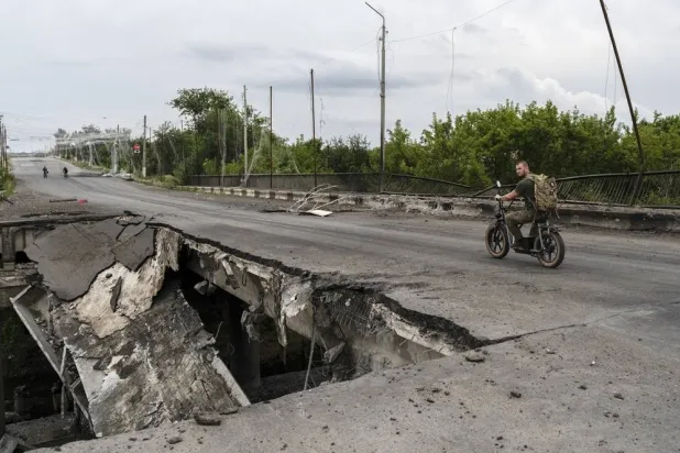 A handout photo made available by the press service of the 93rd Separate Mechanized Brigade of the Ukrainian Armed Forces on 26 July 2026 shows a man ride a scooter on a damaged bridge in Druzhkivka in the Donetsk region, Ukraine, 25 July 2026, amid the ongoing Russian invasion. (EPA/93rd Separate Mechanized Brigade / Handout)