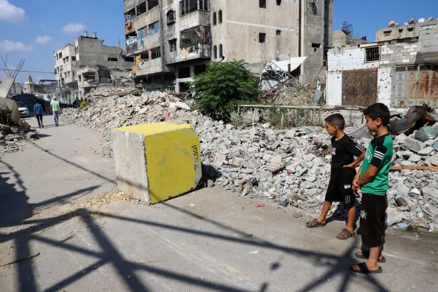 فتيان فلسطينيون ينظرون إلى كتلة خرسانية صفراء تُشير إلى «المنطقة الصفراء» الخاضعة للسيطرة العسكرية الإسرائيلية في حي طفاح بمدينة غزة (رويترز)