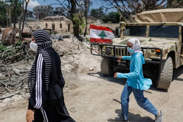 Two women walk past a Lebanese Army armored vehicle during the army’s deployment in the first pilot area in Zawtar al-Gharbiyeh. (Reuters) 