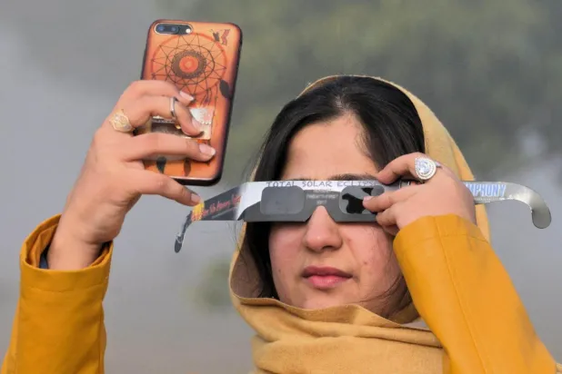 26 Aralık 2019'da İslamabad'daki bir kadın, akıllı telefonuyla güneş tutulmasının fotoğrafını çekerken güneş tutulması gözlüğü kullanıyor (AFP)