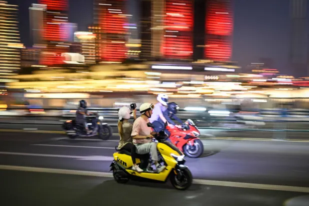 This picture taken on July 20, 2026 shows a woman sitting on the back seat of a motorcycle using mobile phone and lighting equipment to take pictures and videos in Chongqing, southwestern China. (AFP)