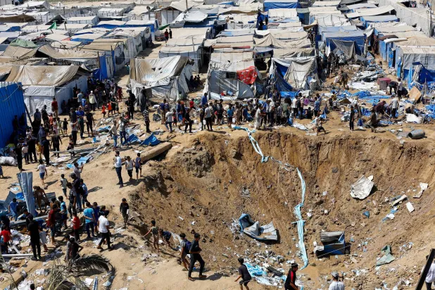 فلسطينيون في موقع ضربة إسرائيلية على مستودع للأدوية قرب خيام للنازحين في دير البلح أمس (رويترز)