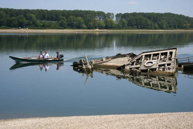 People watch the wreckage of a WWII German warship, emerged due to the drought, in front of Djerdap II, a large dam on the Danube River, between Romania and Serbia, near Prahovo, Serbia, Tuesday, Aug. 4, 2026. (AP) 