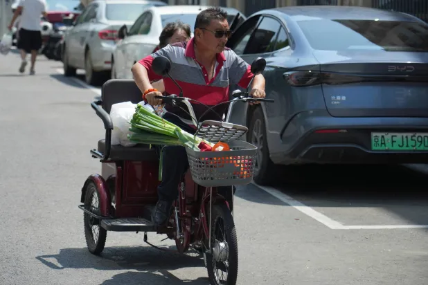 A man rides a tricycle to carry belongings in Beijing Wednesday, Aug. 5, 2026. (AP Photo/Achmad Ibrahim)